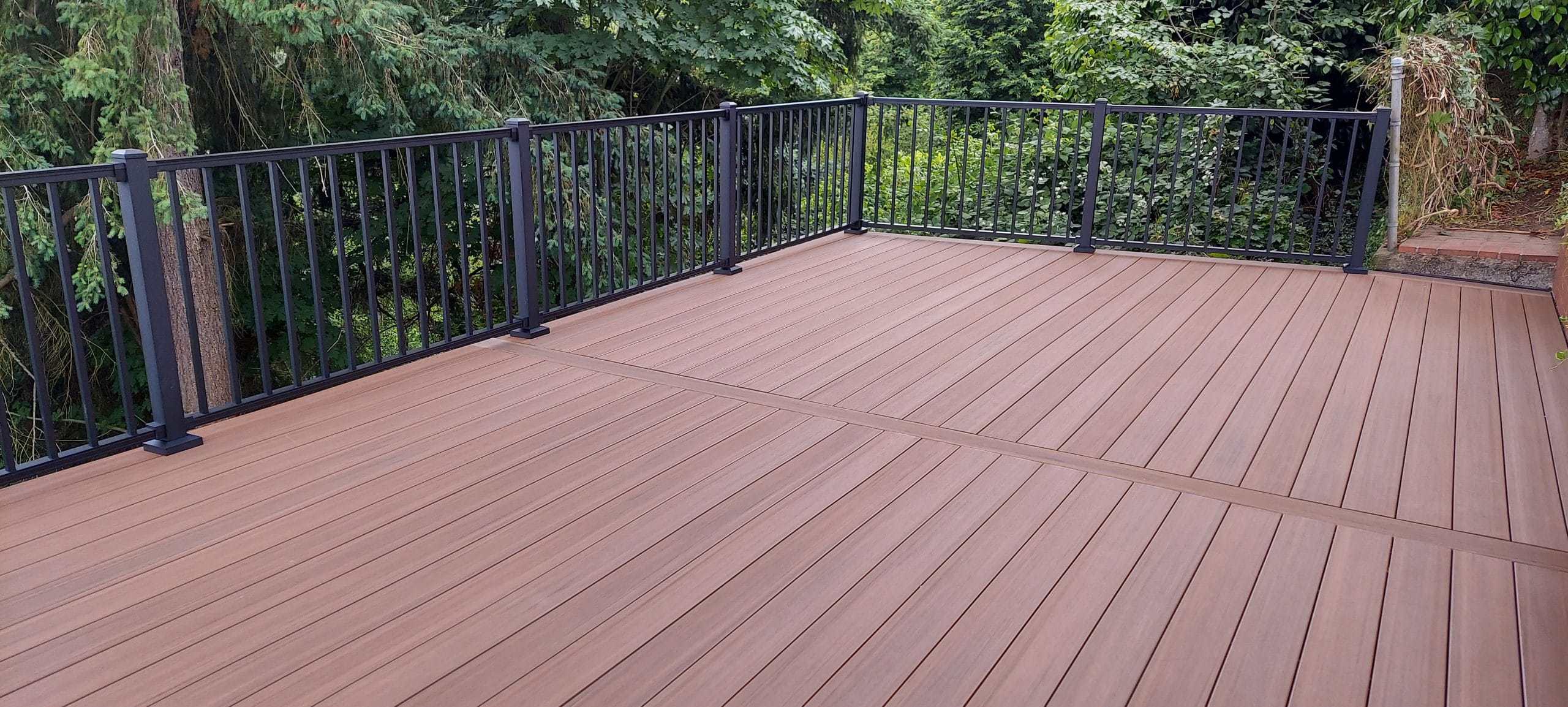Composite deck with black aluminum railings set into Pacific Northwest greenery, built by Father Nature Landscapes