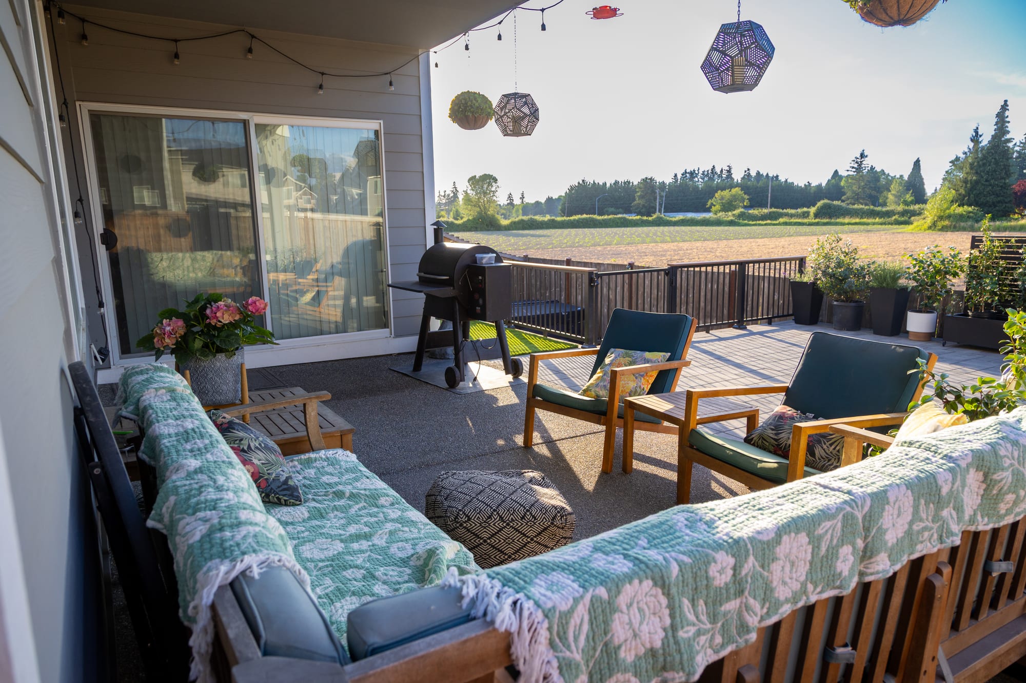 A covered lounge area with a sofa and chairs opening onto the patio and an open field view beyond the railing