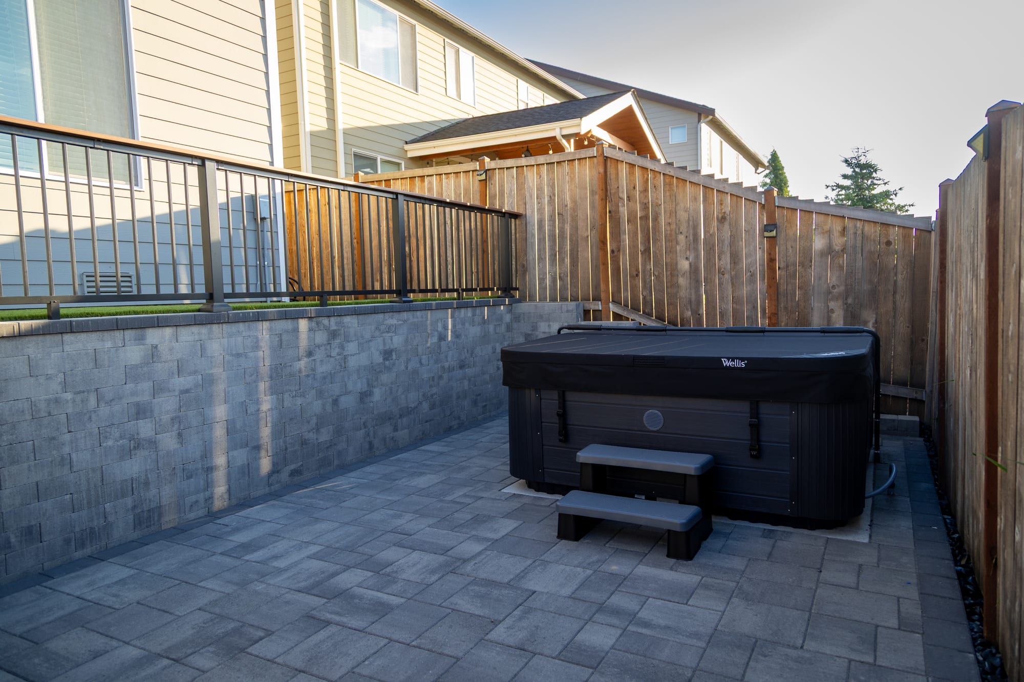 The lower patio with a covered hot tub, enclosed by stone retaining walls and a cedar fence
