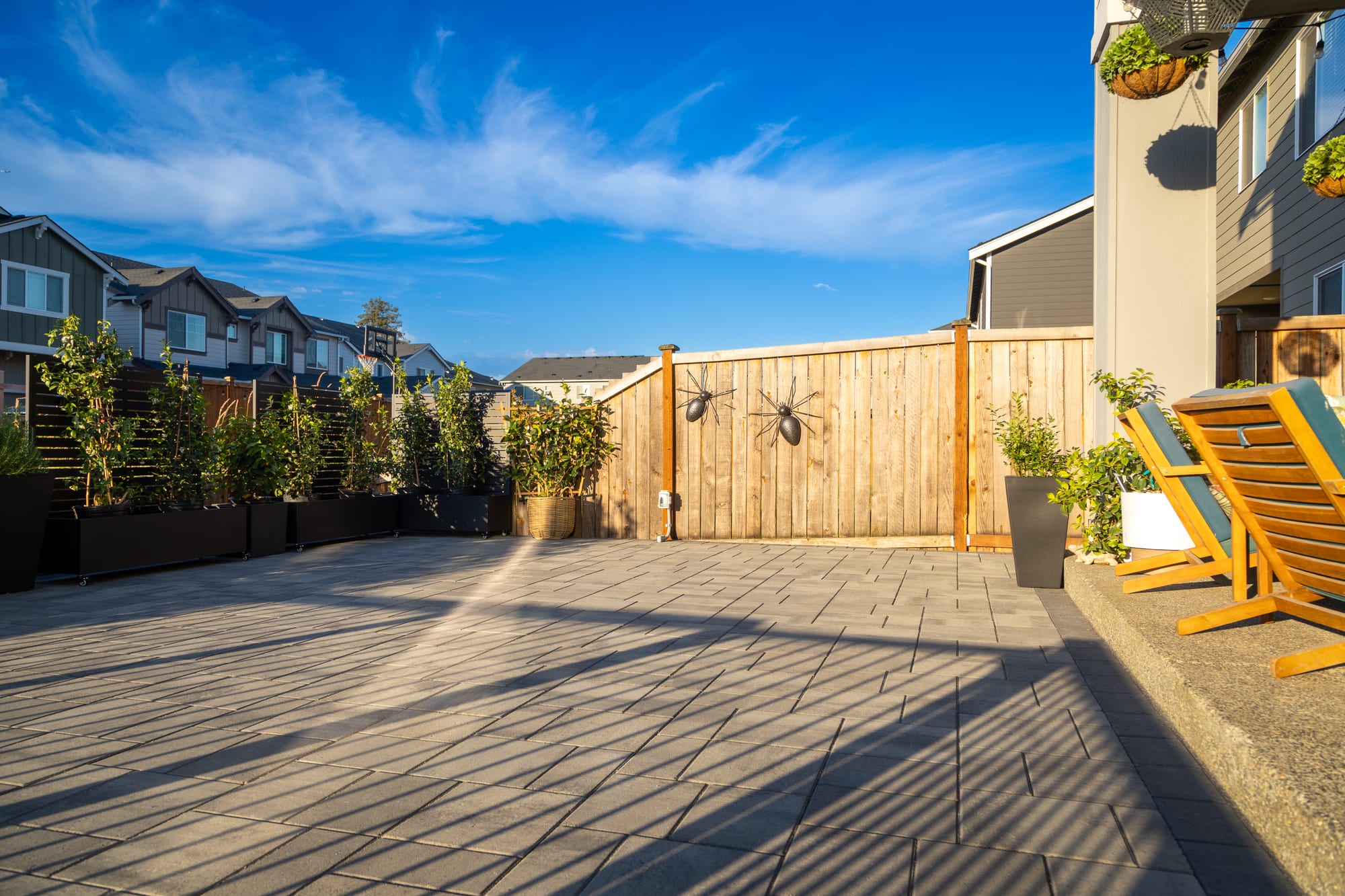 Two wood lounge chairs on the upper paver patio in golden evening light, with the cedar fence and neighborhood beyond