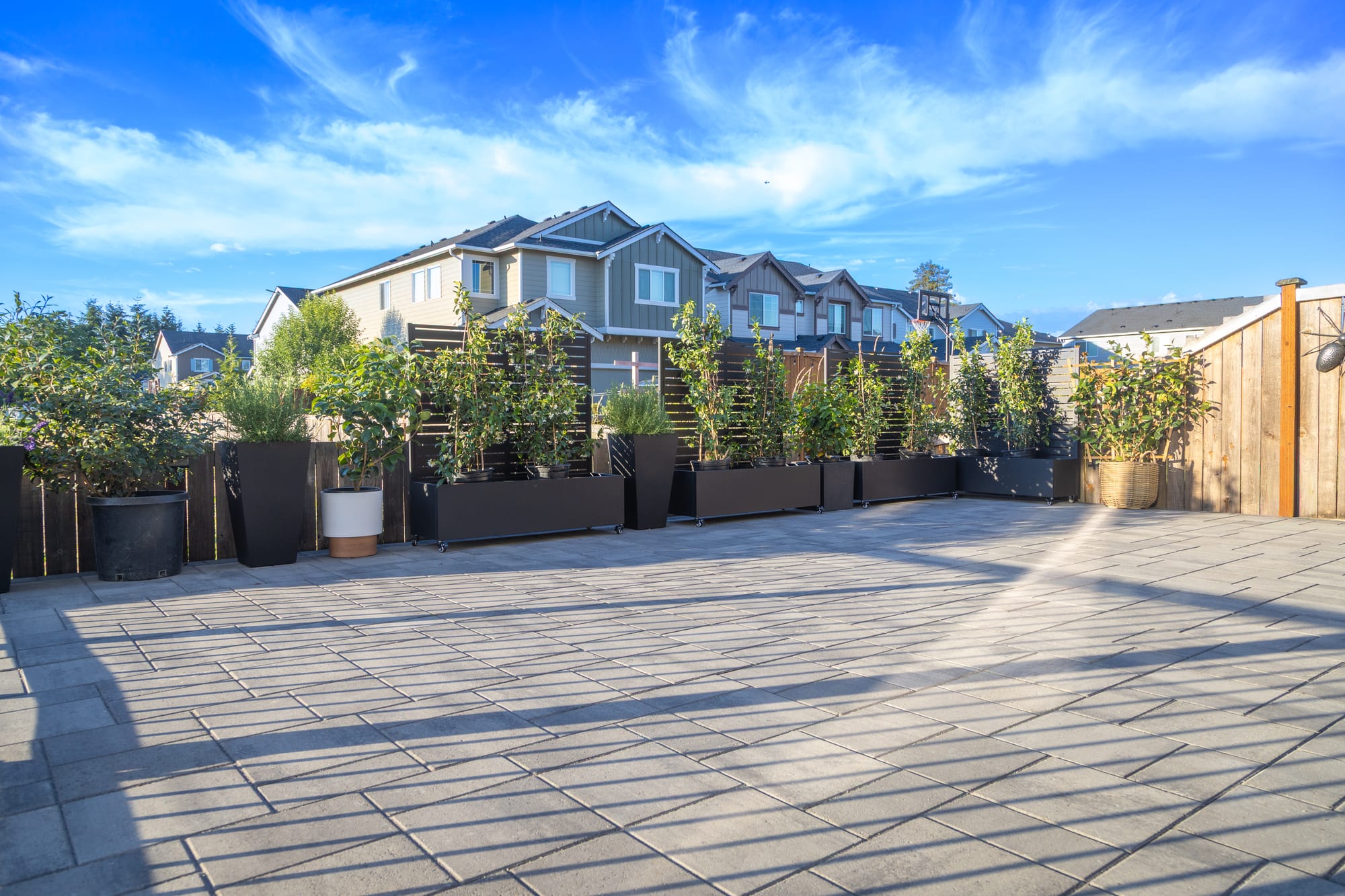 The upper paver patio under a bright sky, edged by a row of planters with privacy screens