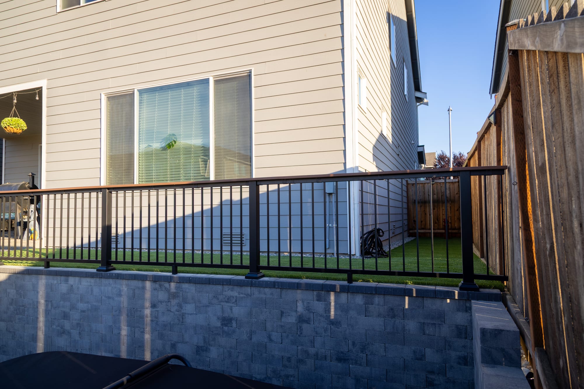 Detail of the aluminum railing anchored to the capped top of a Weston Stone retaining wall, with turf behind