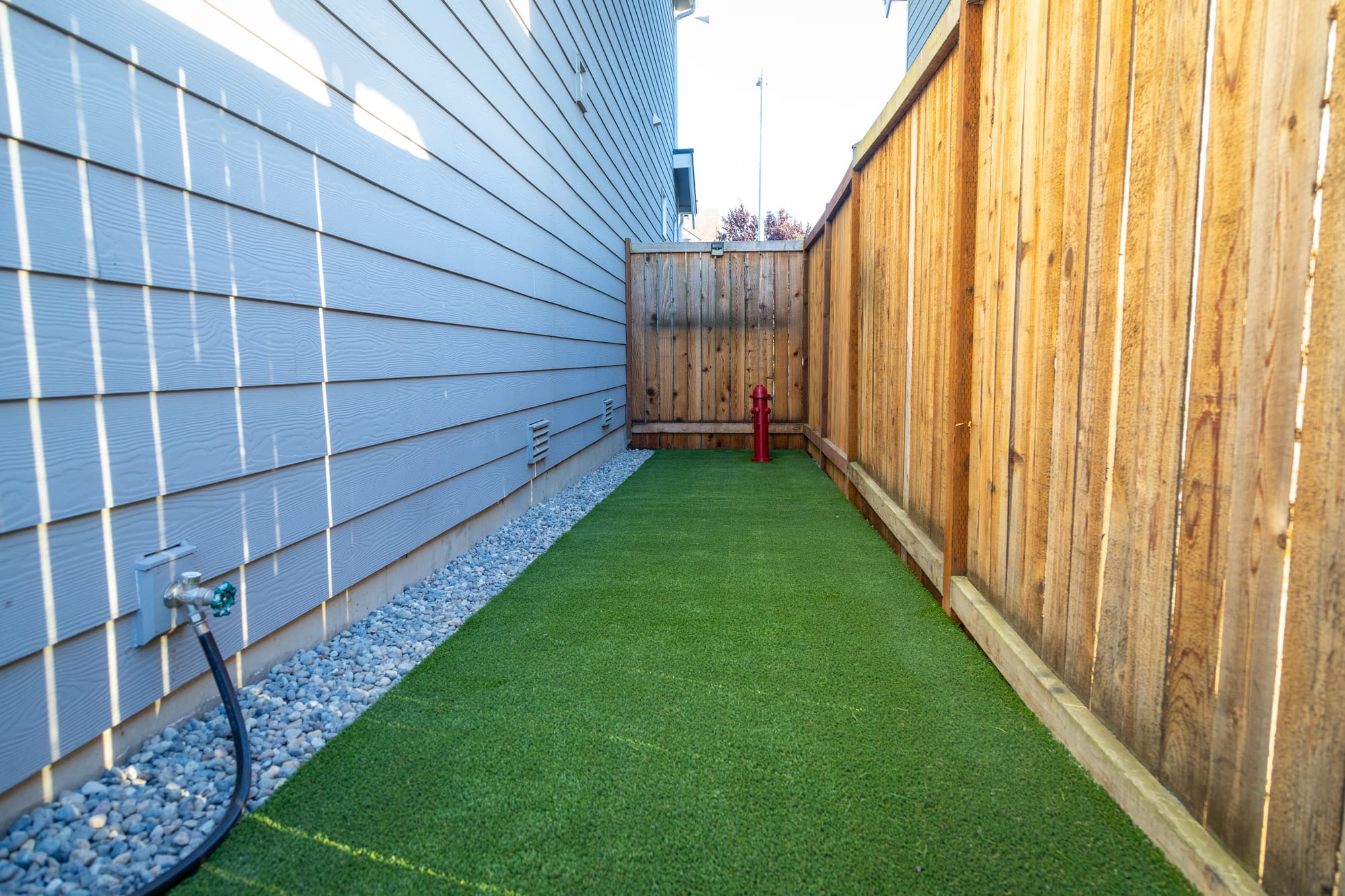 A tidy side yard with a run of synthetic turf, a river-rock border along the foundation, and a cedar fence