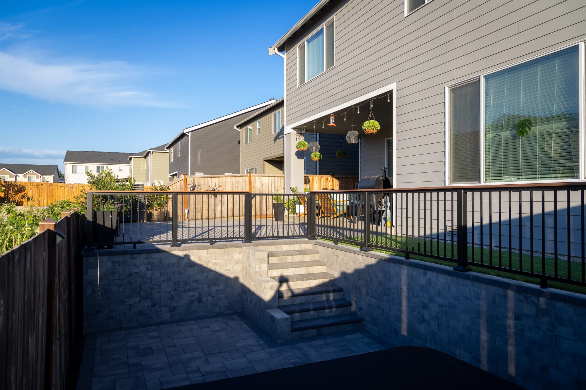 A wide view of the two-level backyard showing the Weston Stone retaining walls, connecting steps, and aluminum railing