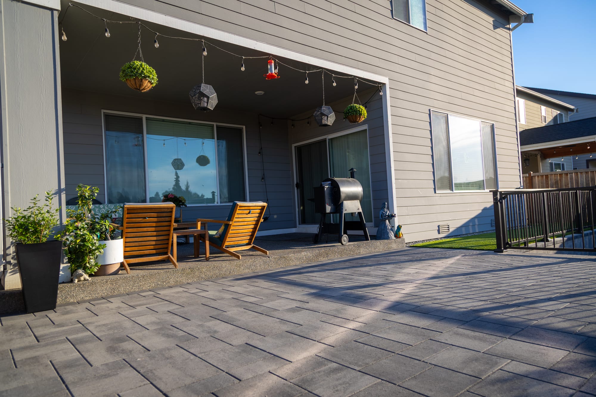 The upper entertaining patio in evening light, with a covered sitting area against the house and a wide Belgard paver floor